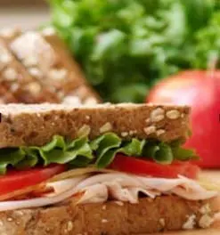 Whole grain sandwich with turkey, lettuce, and tomato, next to an apple and salad greens.
