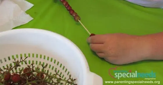 Child threading grapes onto a skewer over a green surface.