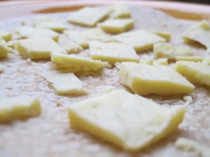 A close-up shot of small, irregularly shaped pieces of cheese scattered on a flatbread.