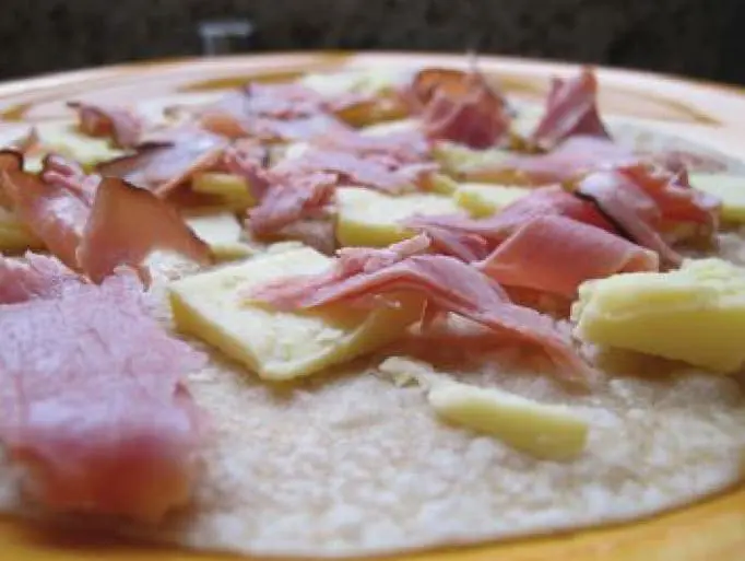 Tortilla pizza with ham and cheese pieces before baking.