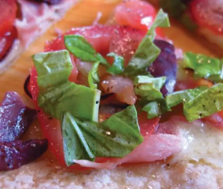 Pizza topped with tomatoes, olives, and basil.