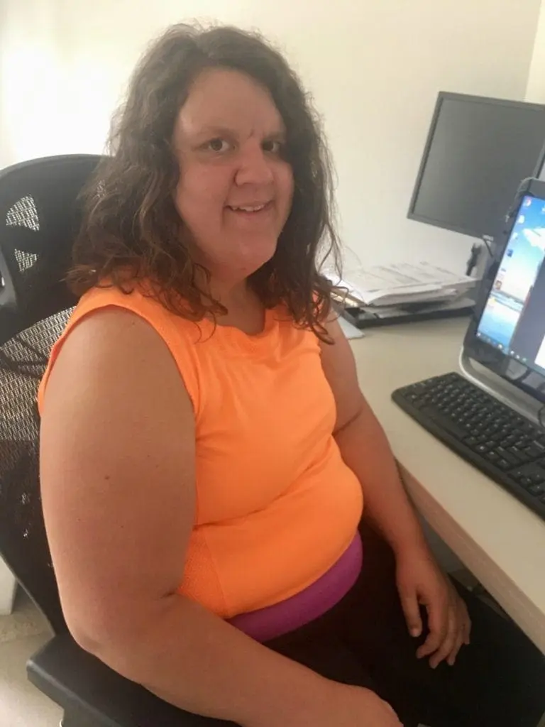 Woman in an orange tank top sitting at a desk with a computer.