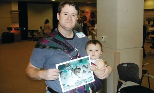 Man in a baby sling holds a picture of a baby.