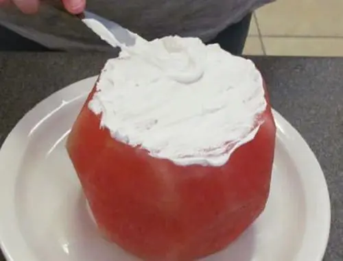 A watermelon cake is frosted with whipped topping.