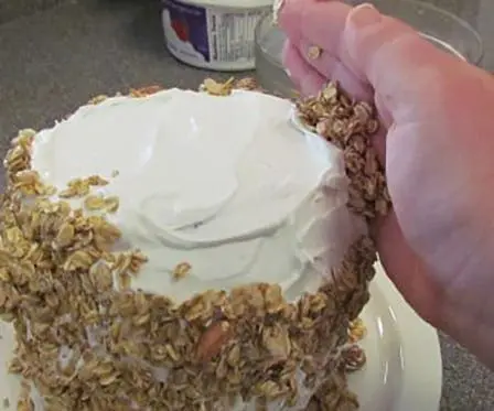 Hand sprinkling granola onto a frosted watermelon cake