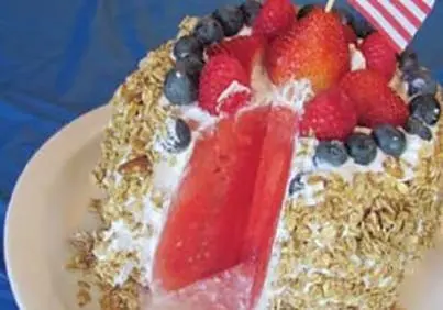 Watermelon cake topped with whipped cream, granola, berries, and a US flag.