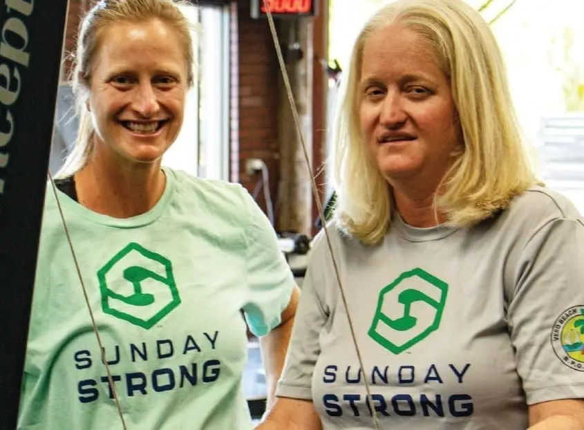 Two women wearing Sunday Strong t-shirts smile at the camera.