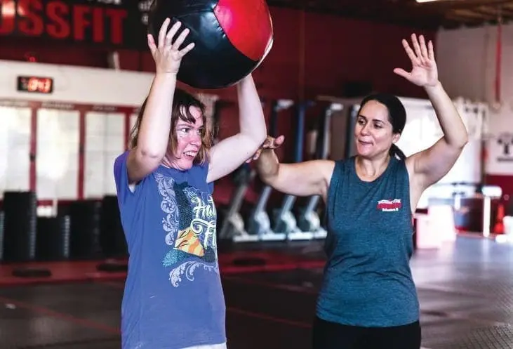 Two women are working out with a medicine ball in a gym.