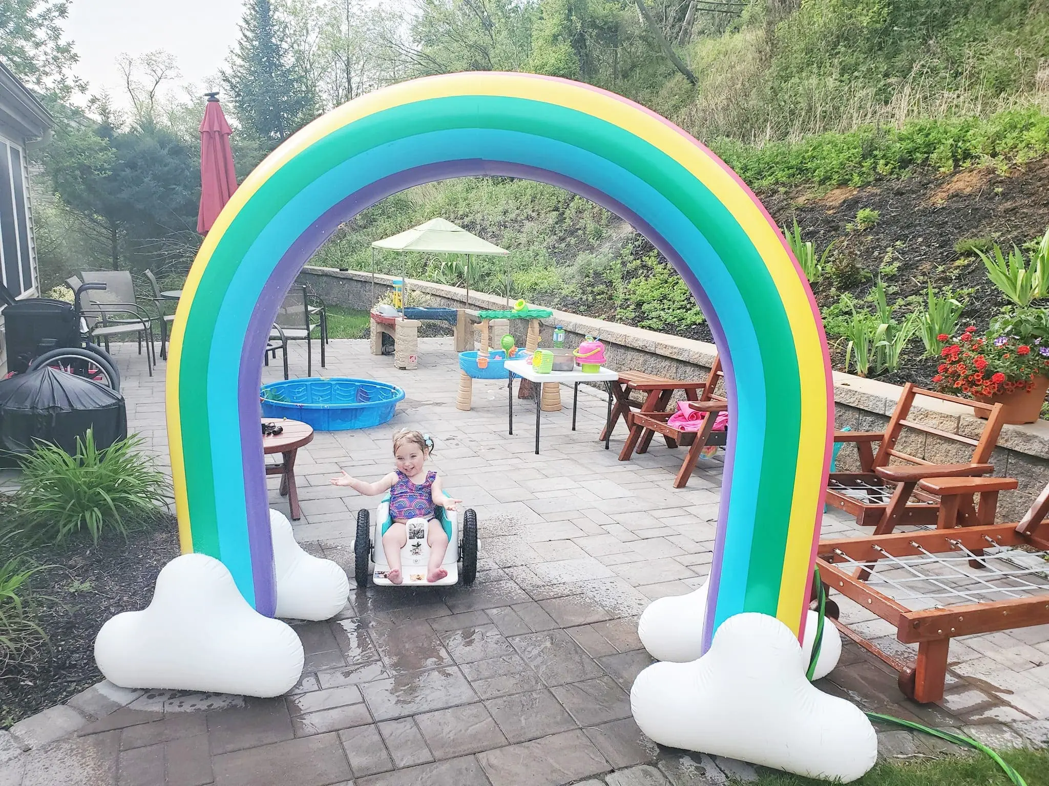 Little girl in a wheelchair playing under a rainbow sprinkler