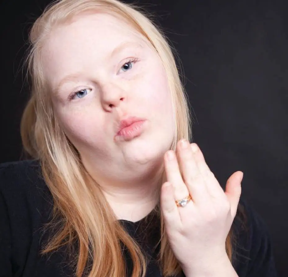 Angel with blonde hair and a black shirt puckers her lips and blows a kiss.