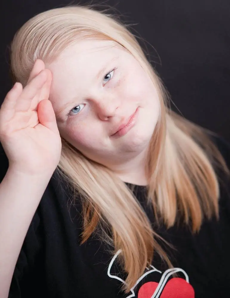 Angel with blonde hair and a black shirt, resting her forehead on her hand.