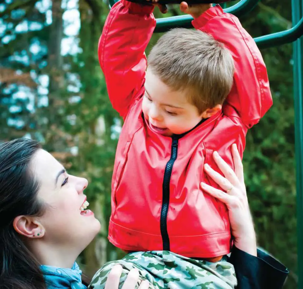 Connor smiles while being held by a woman at a playground.