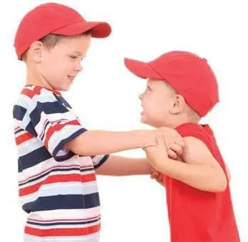 Two young boys wearing red baseball caps and looking at each other.