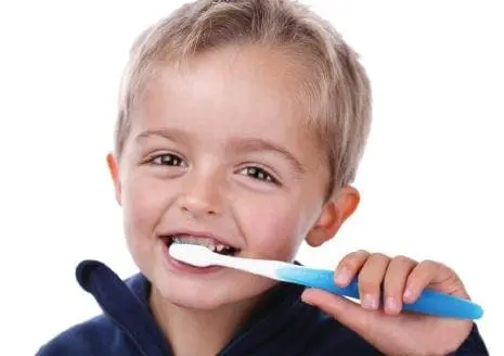 A young boy smiles while brushing his teeth.