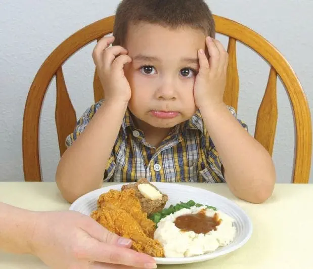 Young boy with hands on his head looking at a plate of food