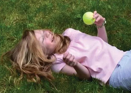 A young girl lies on green grass holding a yellow ball.