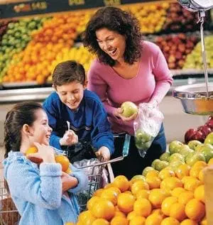 A mother and her two children happily shop for fruit in a grocery store.