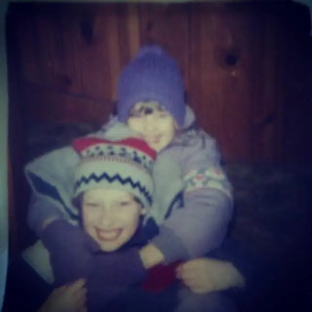 Two children wearing winter hats hug each other.