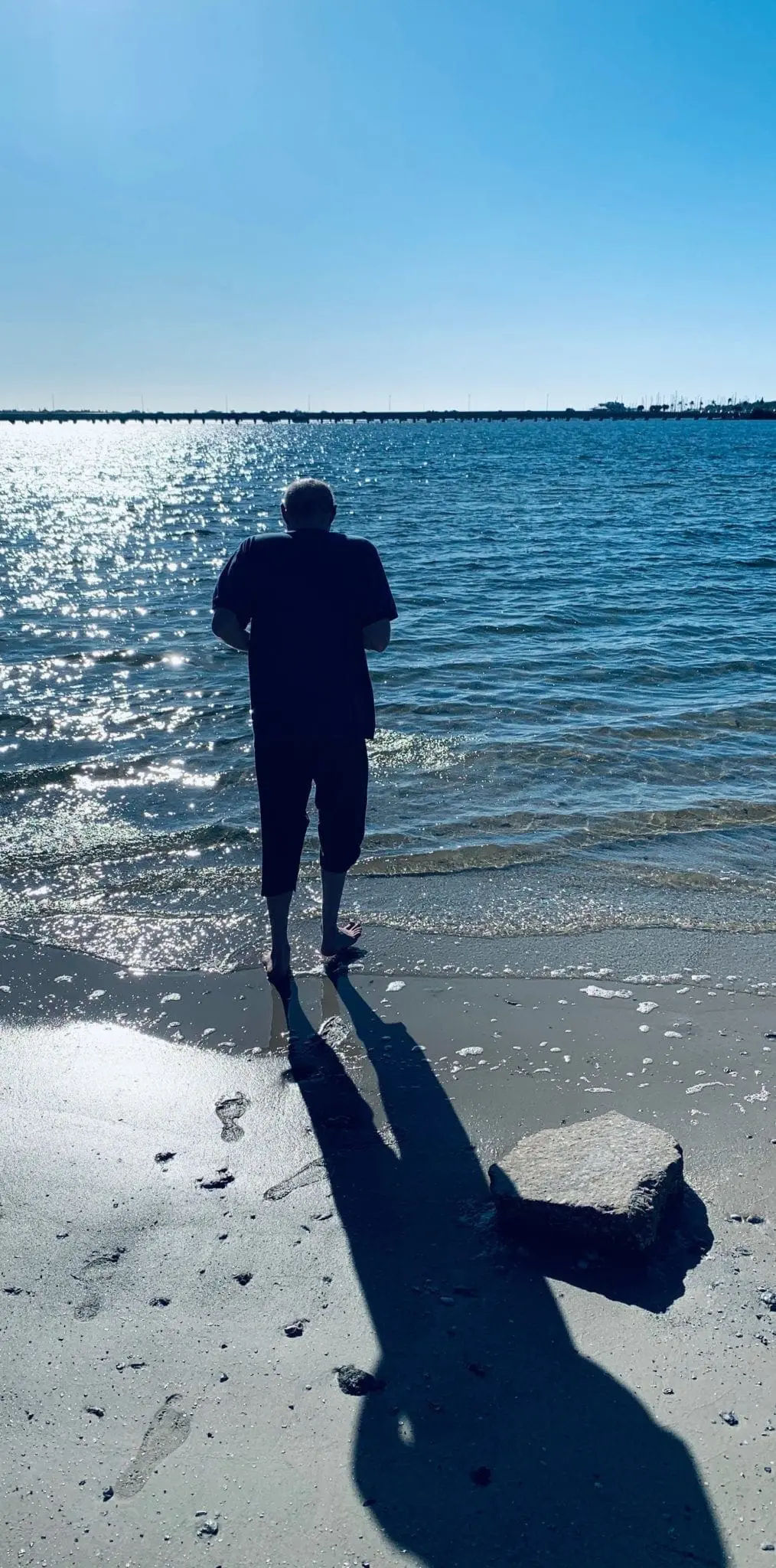 Person stands at the edge of the water on a sunny day.