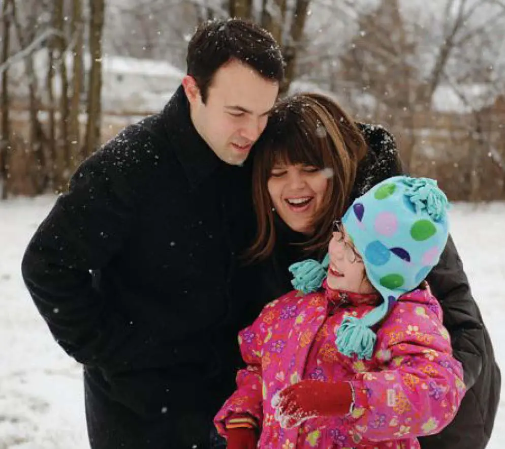 Emma smiling while standing in the snow with her parents.