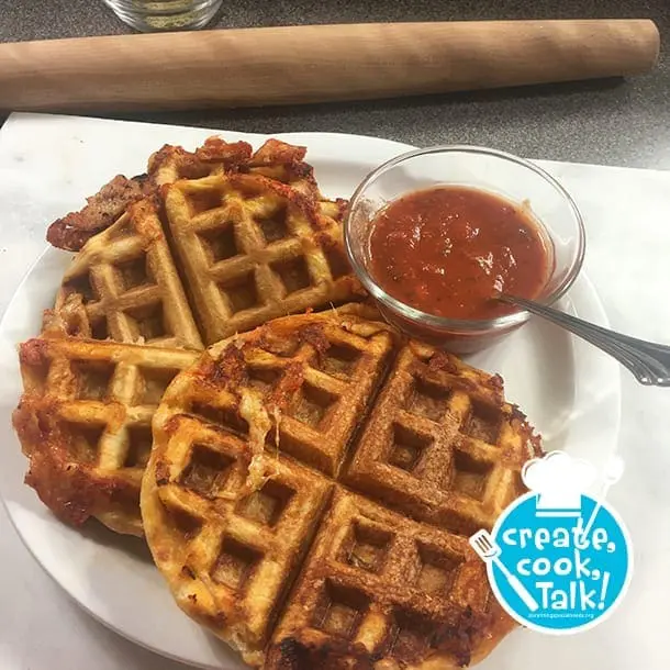 Four golden-brown waffles served with a side of red sauce.