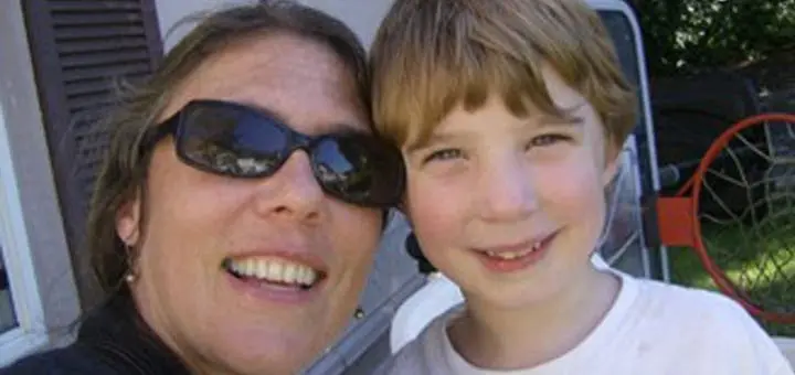 A woman wearing sunglasses and a young boy smile for the camera.