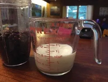 Measuring cup with milk next to a blender filled with black beans.