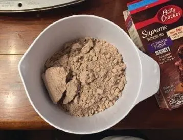 Brownie mix in a white mixing bowl next to a box of Betty Crocker Supreme Brownie Mix.
