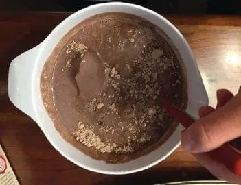 Mixing brownie batter and chocolate chips in a white bowl with a red spoon.