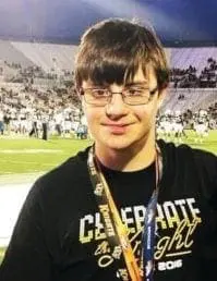 College student wearing a black shirt and glasses, with a football stadium in the background.