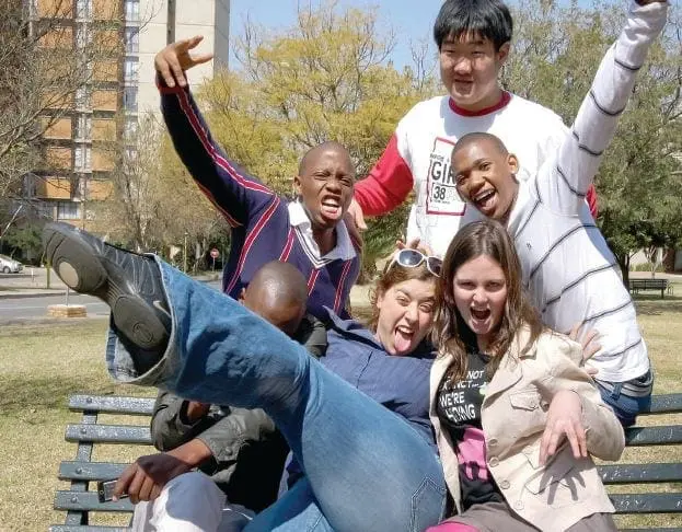 Five young adults posing energetically on a park bench.