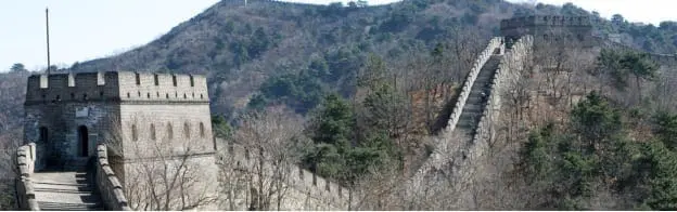 The Great Wall of China snakes over a forested mountain range.