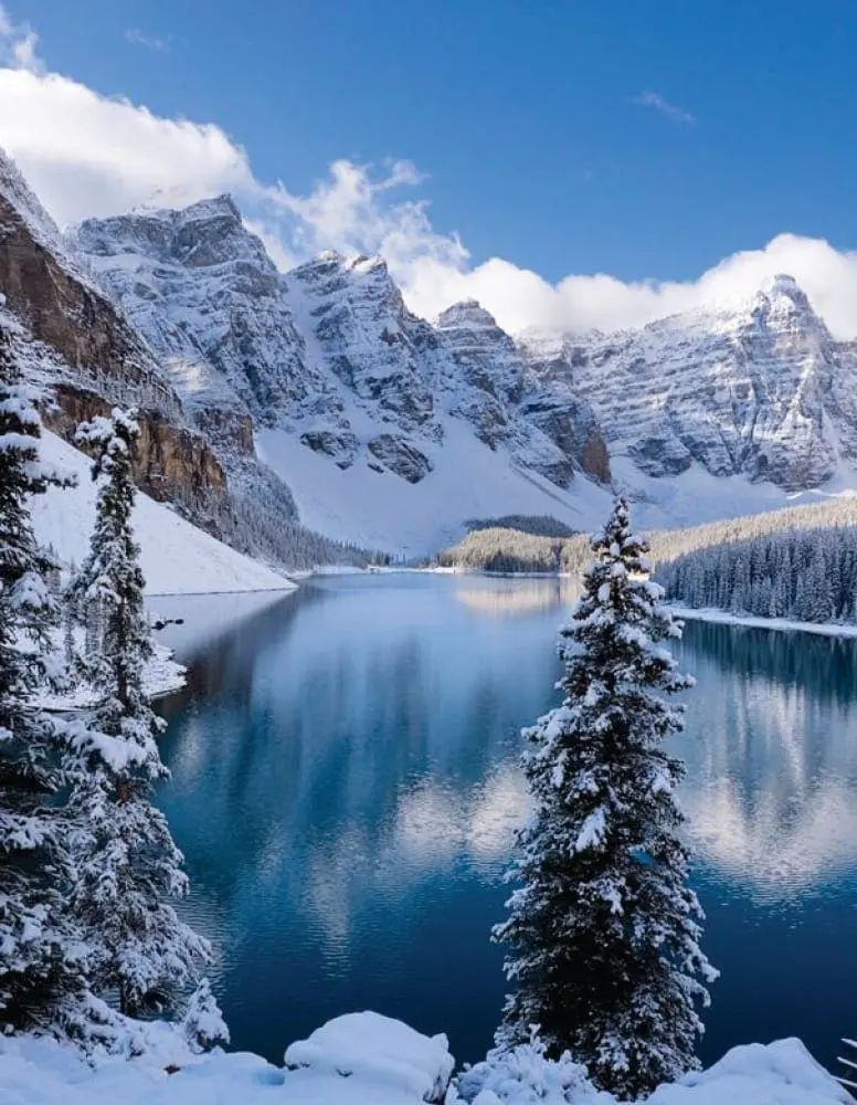 Snow-covered mountains reflect in the calm waters of Lake Louise, Alberta, Canada.