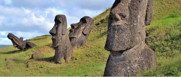 Moai monolithic statues on a grassy hillside under a cloudy sky