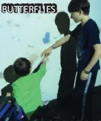 Two boys reach toward a projected image of butterflies on a wall.