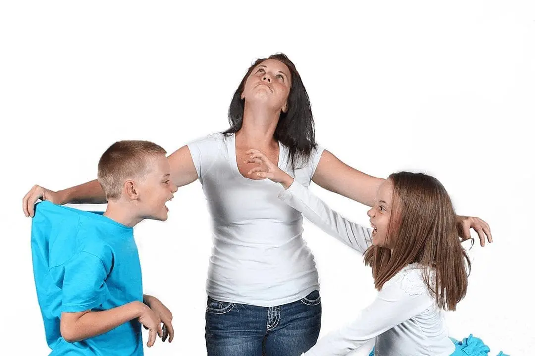 A woman with her arms outstretched is surrounded by two children who appear to be pulling at her.