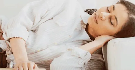 A woman sleeps peacefully on a couch, her head resting on her arm.