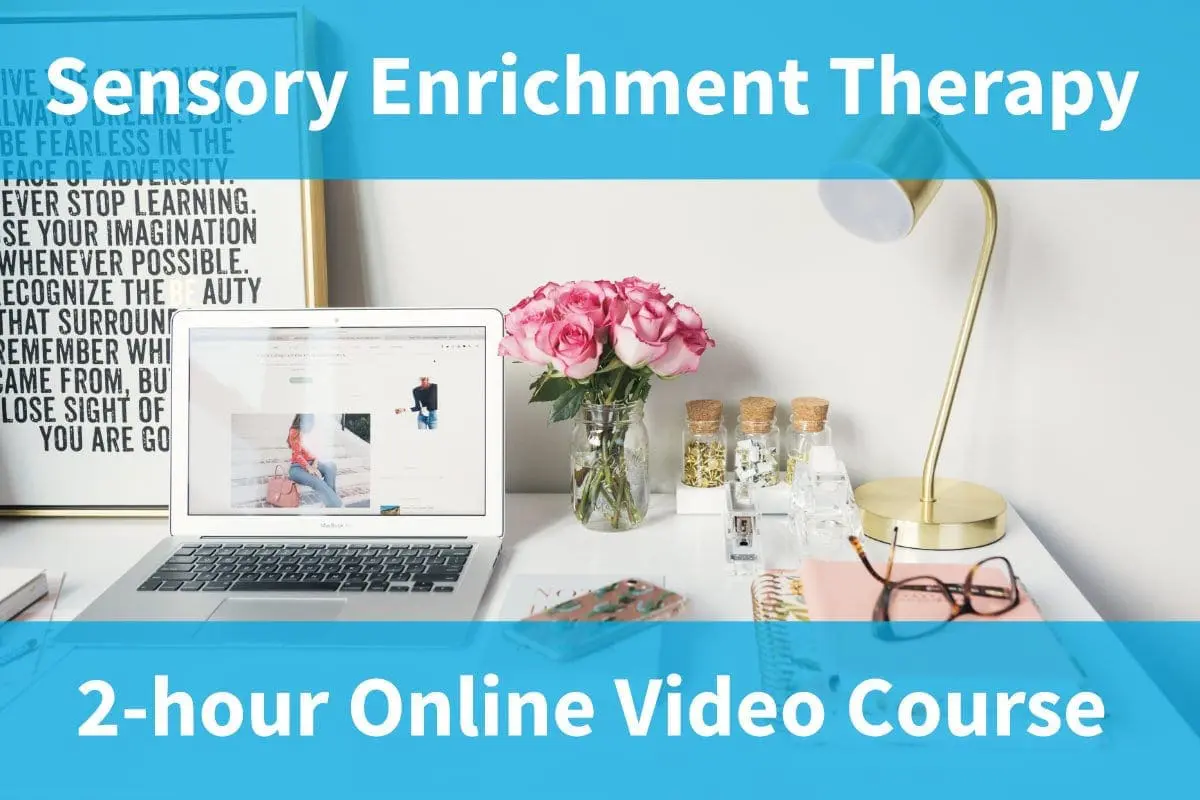 A laptop, flowers, and a lamp are on a table with a sign that says "Sensory Enrichment Therapy.