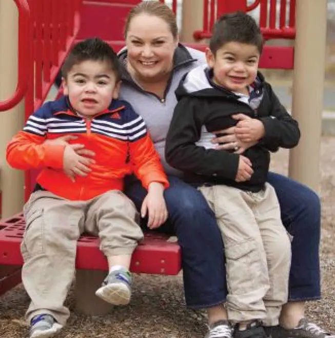 Woman with two young boys sitting on a red playground structure.