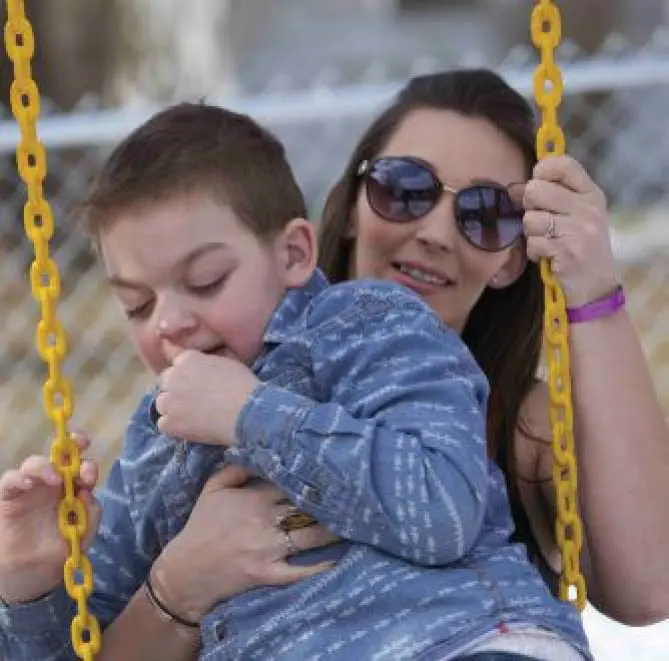 Natalie holding her son Silas on a playground swing.