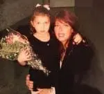 A woman hugs a young girl holding a bouquet of flowers.