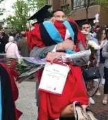 Person in graduation regalia hugging a bouquet of flowers.