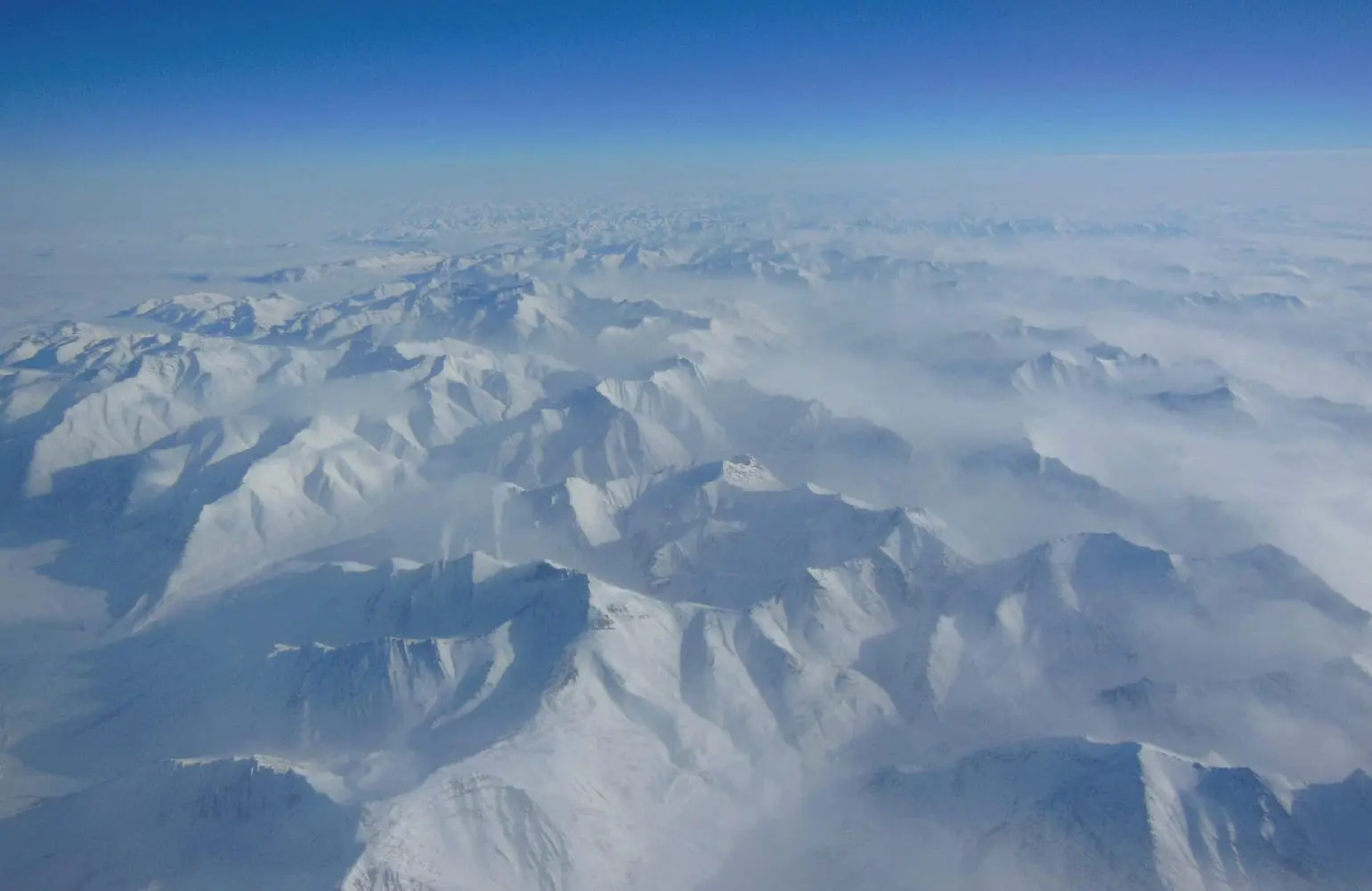 Snow-covered Alaskan mountains seen from above under a clear blue sky.