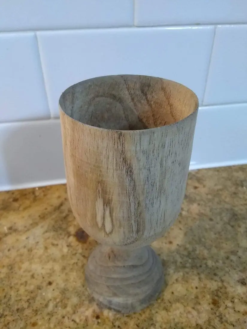 Wooden goblet with a textured surface on a speckled countertop.
