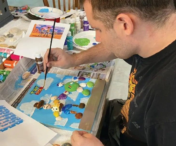 Adam Flasterstein painting a canvas with shells and paint.
