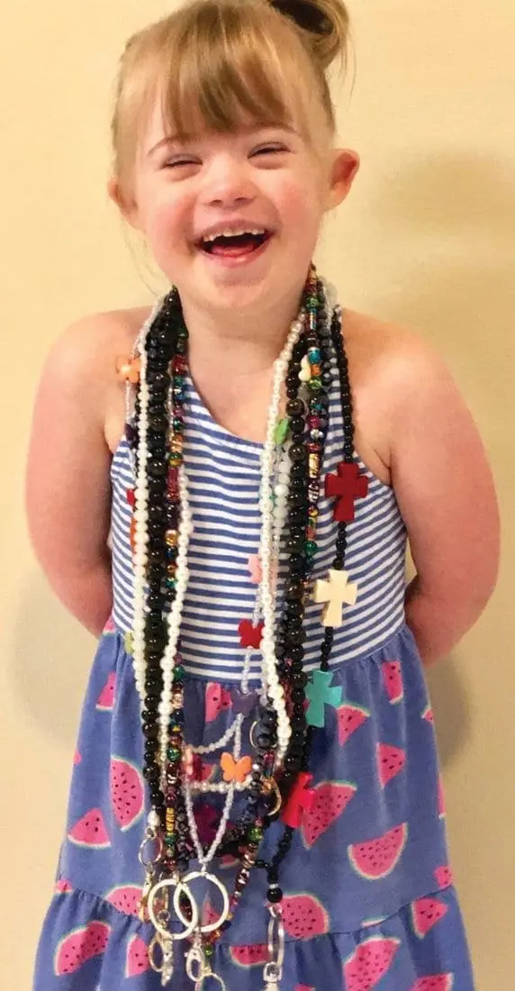 Lila Morrow smiling, wearing a striped top and watermelon-print dress, with beaded necklaces.
