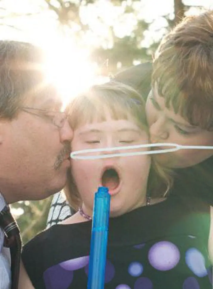 Madison with a bubble wand being kissed by two people