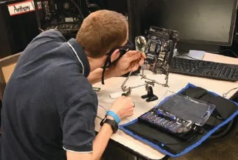 Cody works on a computer motherboard with a magnifying glass.