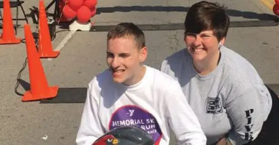 Two people smile at the camera at an outdoor event with orange cones.