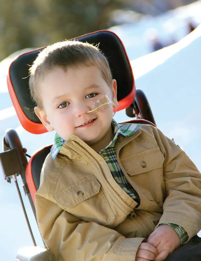 Lukas smiling in a wheelchair with a nasal cannula.